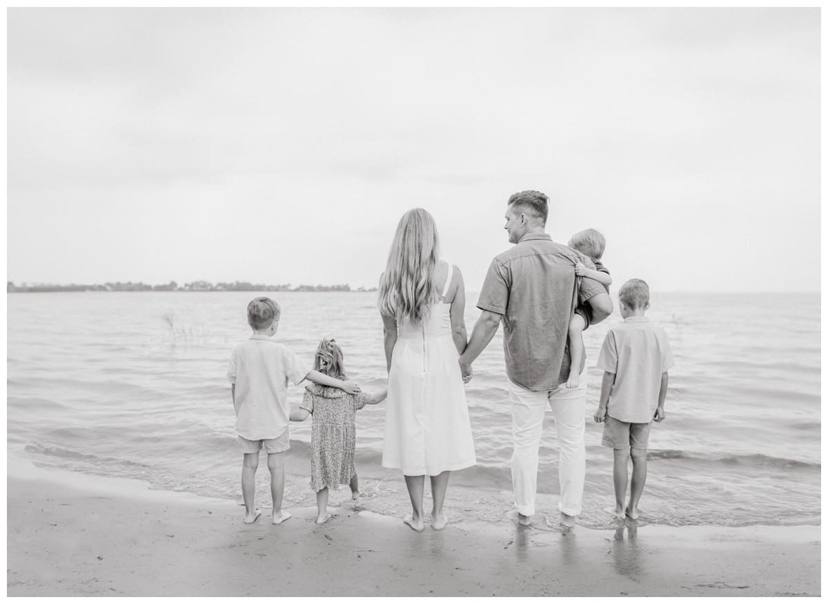 Black and white photo of a family holding hands and facing the water together, a timeless example of what is lifestyle photography and capturing connection.