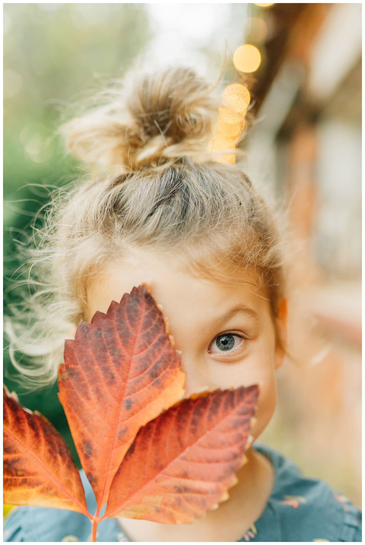 Young girl peeks through a large red fall leaf, smiling playfully during a family session with Edmond family photographer Haley Kinzie Photography.