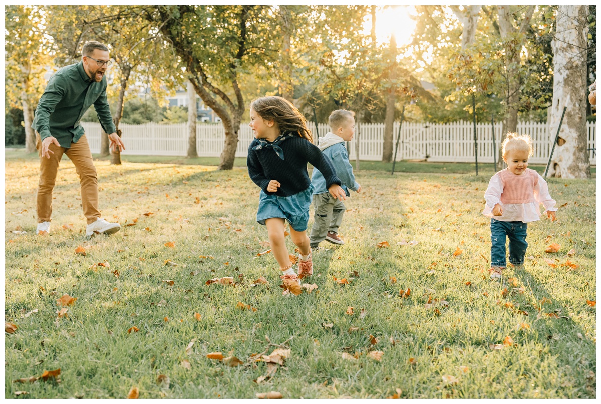 Children run through a grassy field with their dad during golden-hour fall photos, wearing layered fall outfits perfect for Edmond family sessions.