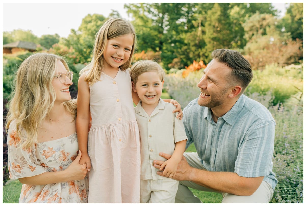 How to Dress for Spring or Summer Family Photos: Family of four in coordinating pastel outfits playing and sitting in a lush green park.