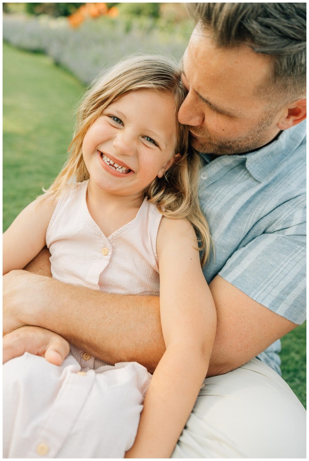 How to Dress for Spring or Summer Family Photos: Father holding daughter in light pink dress, both smiling in warm evening light.