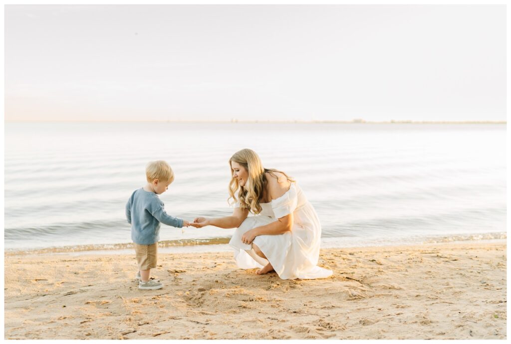 mom showing toddler son what is in her hand at beach in photo session