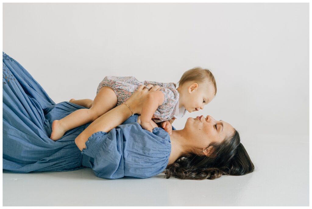 mom laying on back holding her one year old girl giving her a kiss in ren space studio session 