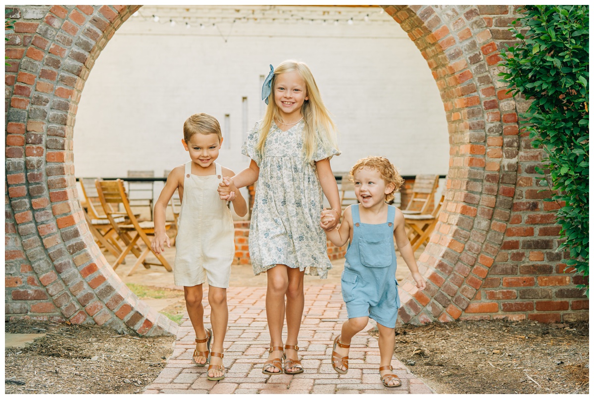 three siblings running towards photographer Haley Kinzie through a brick walkway