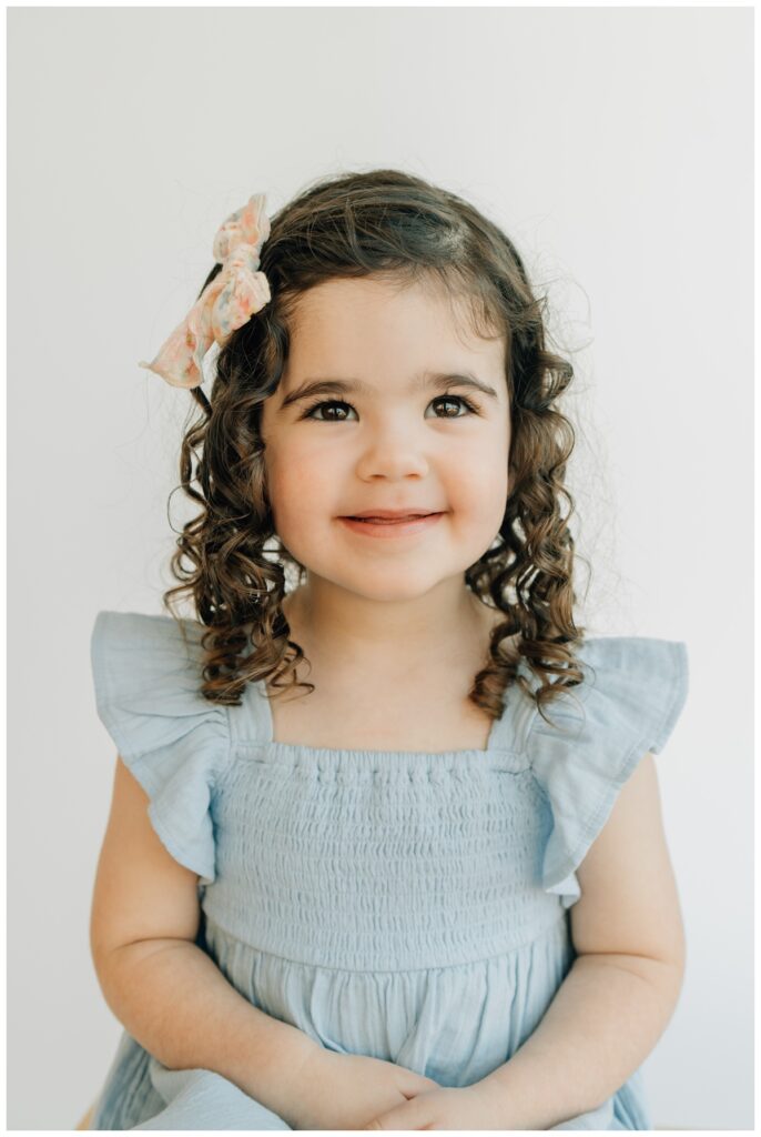 toddler girl with curls smiling for preschool portraits 