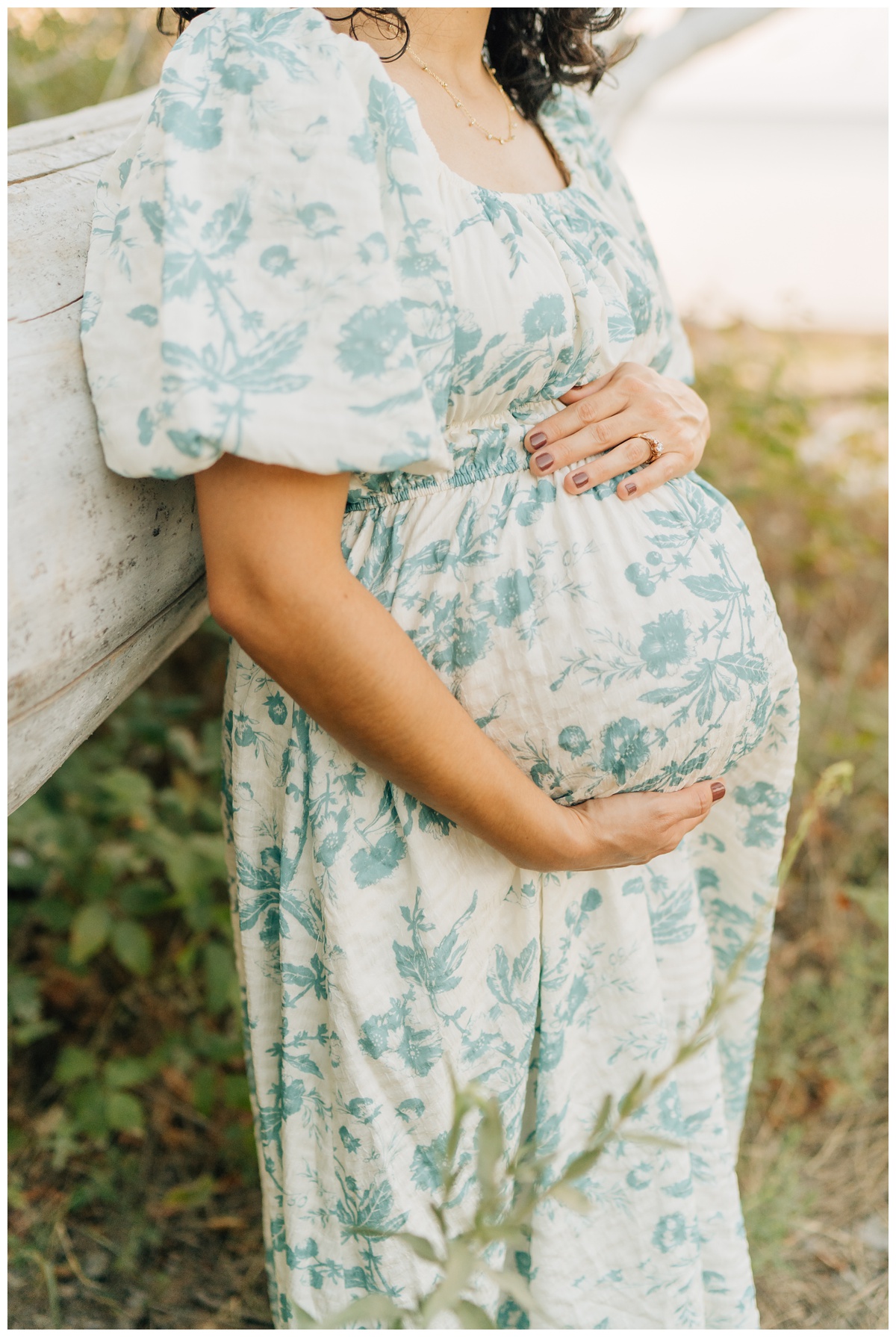 mom leaning against branch with hand on baby bump at beachside maternity session at Lake Hefner in OKlahoma 
