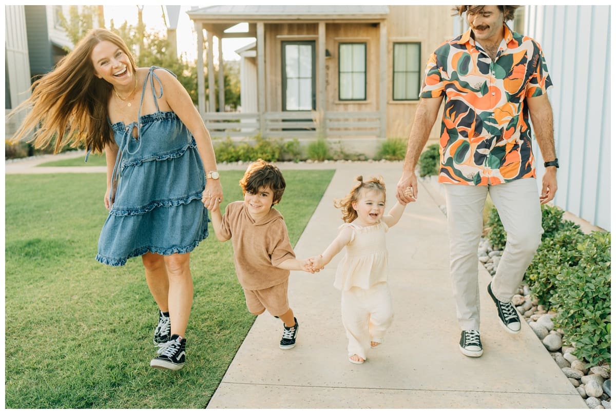 Family poses walking hand in hand outdoors, laughing together on a sunny day.