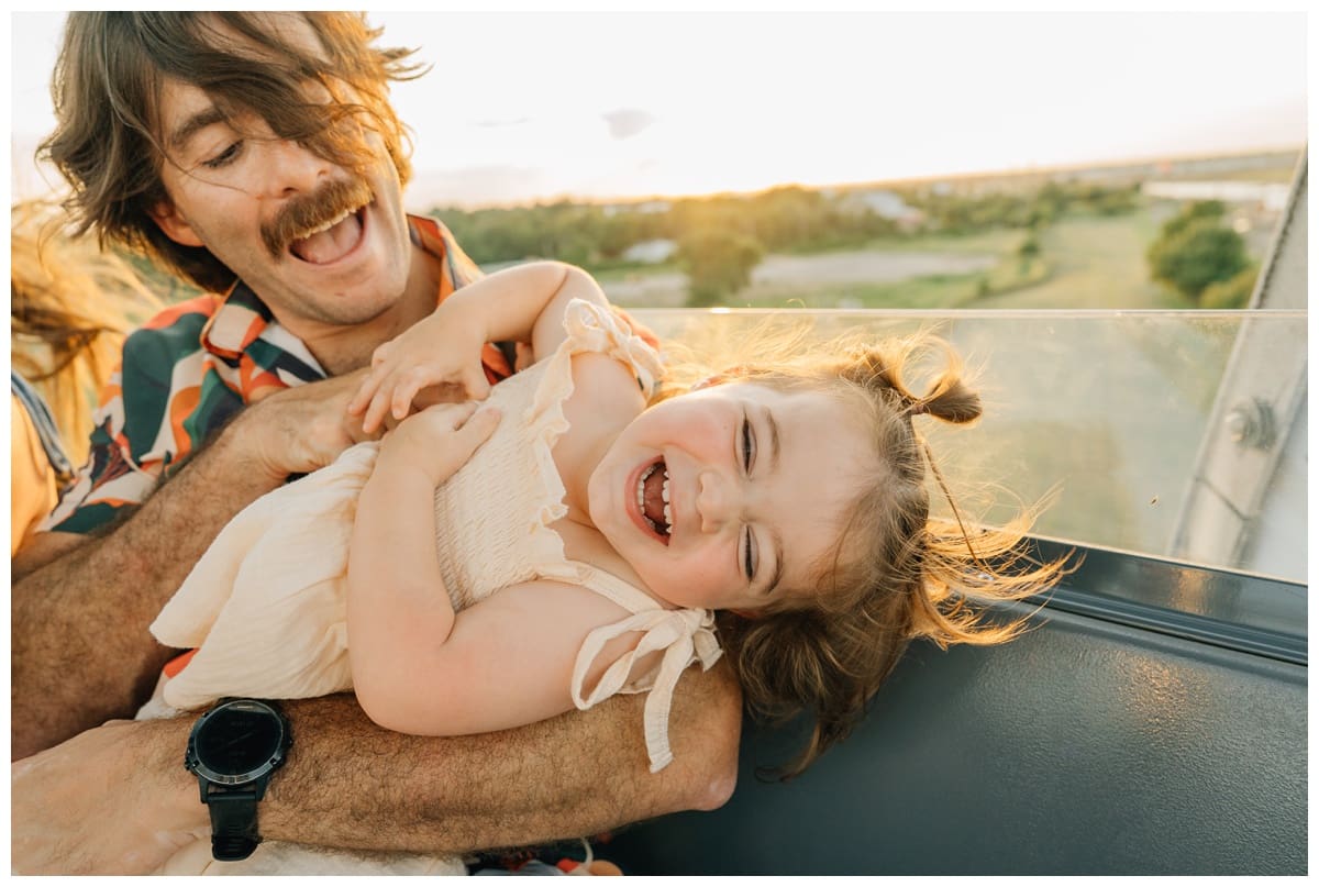 Joyful family pose in a Haley Kinzie Photography session, with a father holding his giggling daughter at sunset.