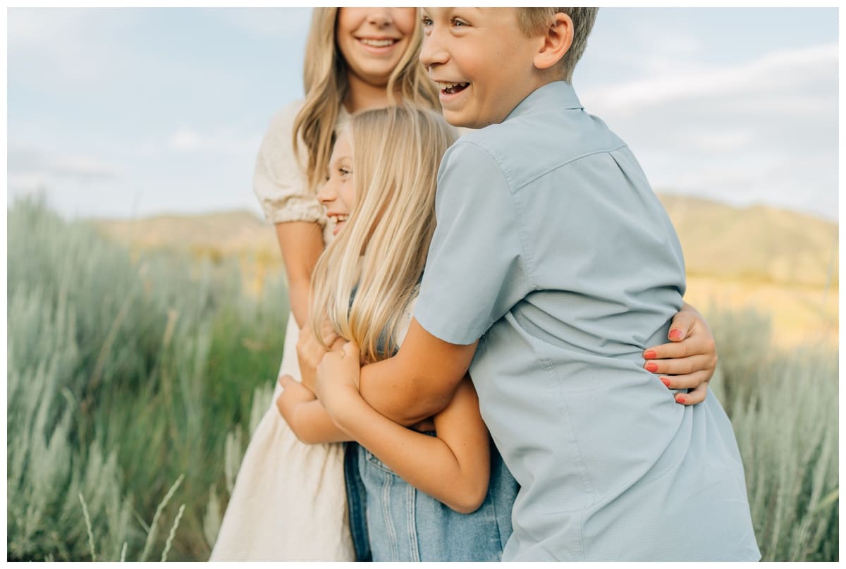 Siblings hug tightly in a playful family pose outdoors during a family session with Haley Kinzie Photography.