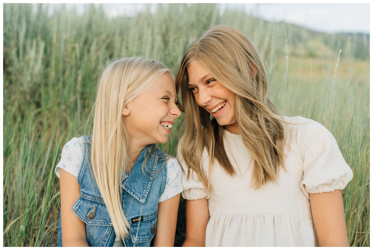 Sisters laugh together in the grass, captured in a sweet family pose during a Haley Kinzie Photography session.