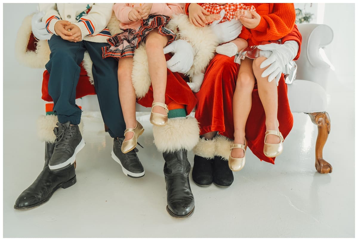 Children in festive outfits sit with Santa and Mrs. Claus, showing sparkly shoes and plaid skirts during holiday Santa Minis with Haley Kinzie Photography. 
