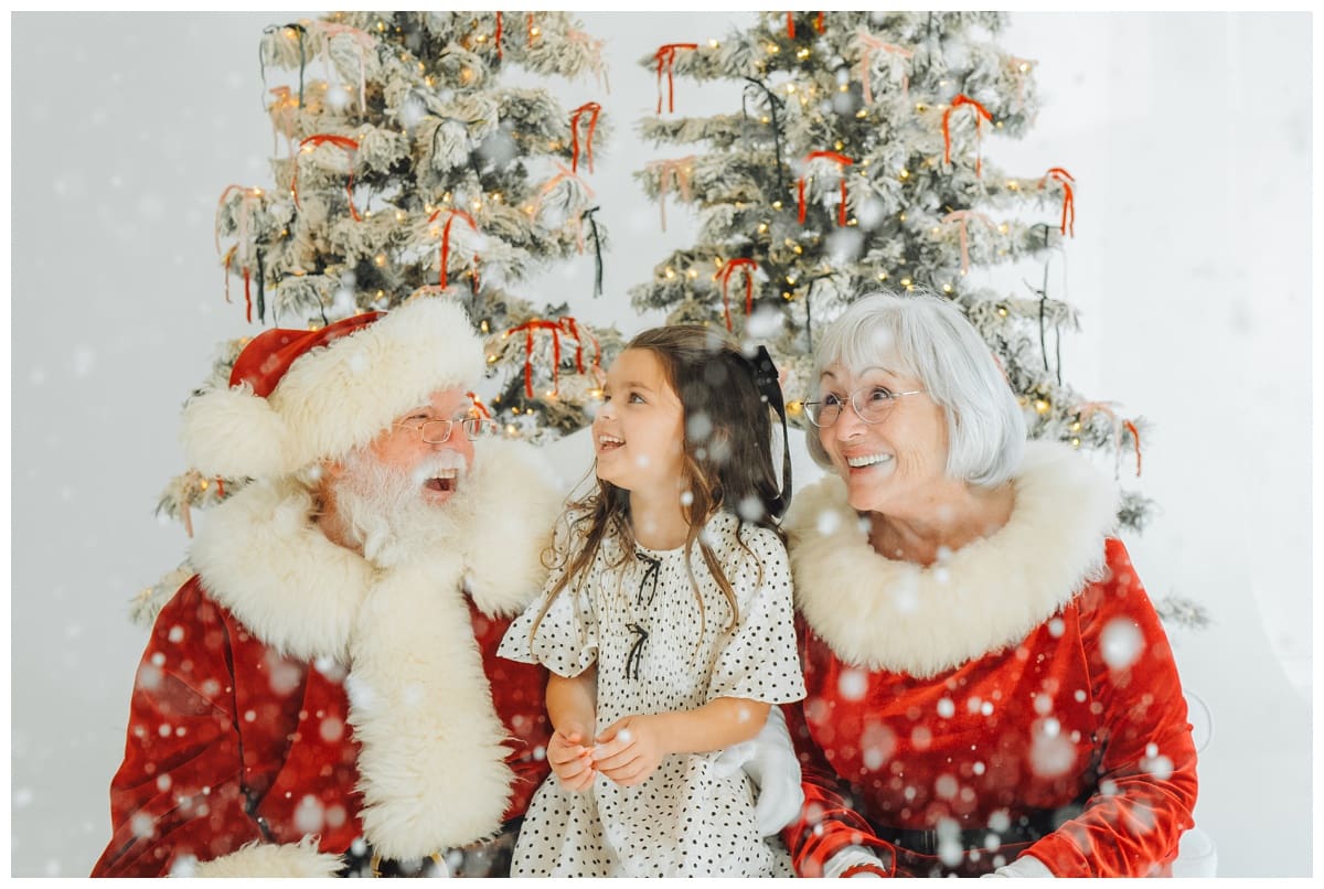 Santa and Mrs. Claus laugh with a girl in a polka dot holiday dress as snow falls during magical Santa Minis.