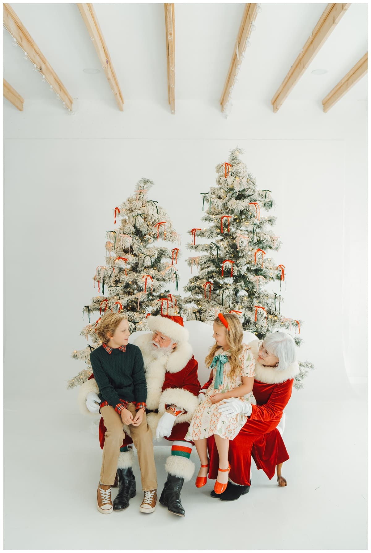 Mr and Mrs Claus chatting with two elementary children in white studio photo sesison with Haley Kinzie