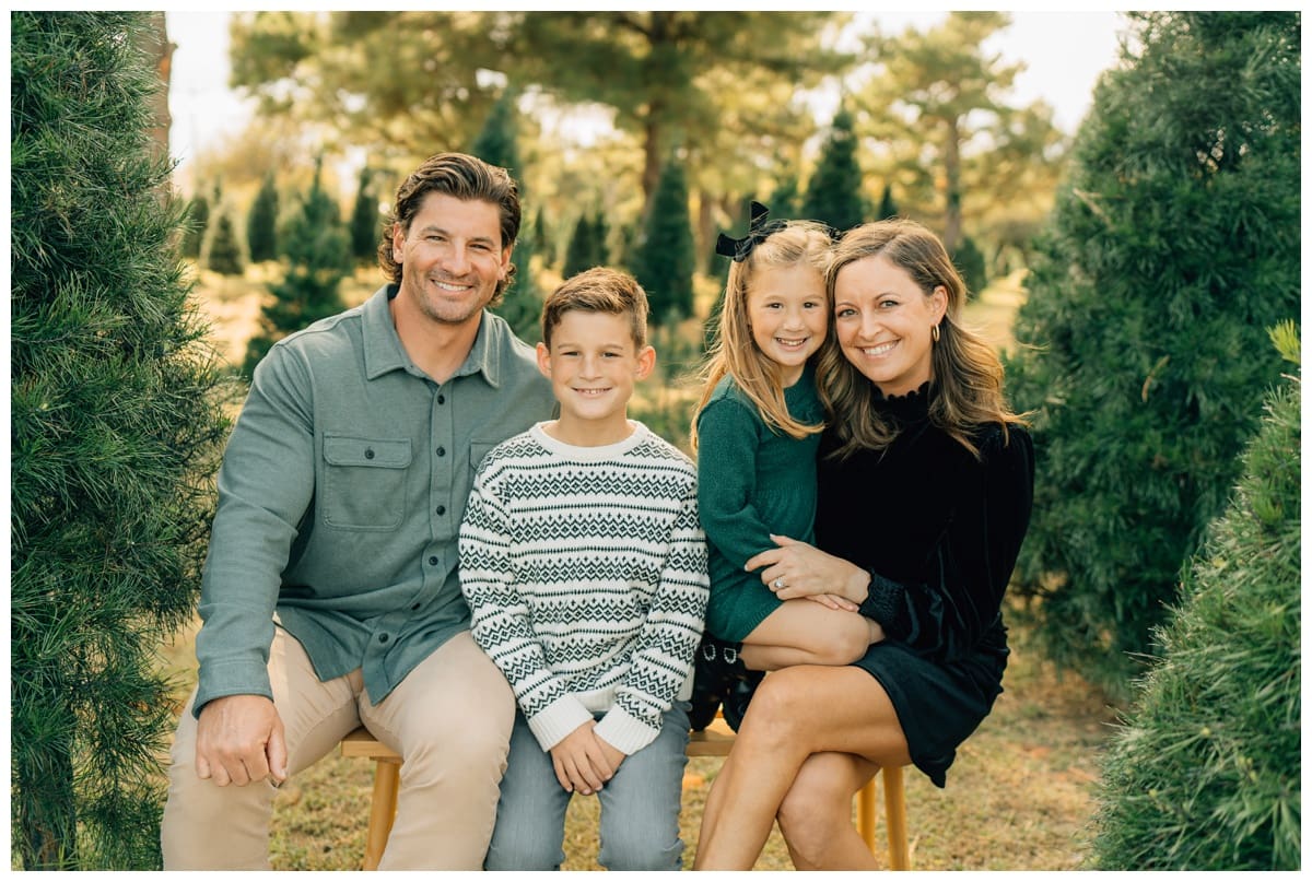 Family of four at Christmas tree Farm with evergreen-toned family Christmas photo outfits